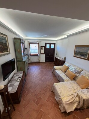 Ein Wohnzimmer mit einer Sofagarnitur, einem Fernseher, einem Schrank und einer Tür zu einem anderen Raum.