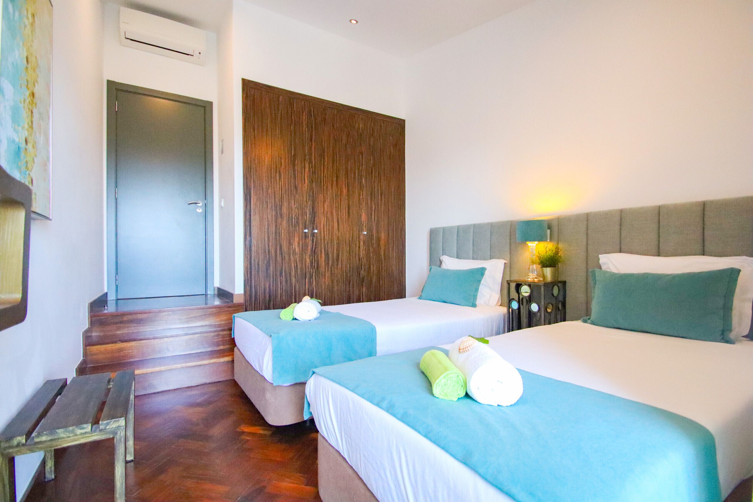 A hotel room with two beds, a wooden bench, a wardrobe, and a staircase.