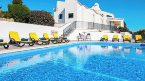 Una piscina con lettini, una scalinata che conduce a un edificio e un cielo azzurro terso.