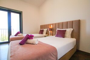 Twee aangrenzende hotelkamers met bedden, nachtkastje, lamp en een raam met uitzicht.