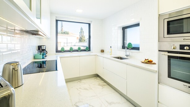 Eine moderne Küche mit weißen Schränken, einem Einbauofen und einem Fenster mit Blick ins Freie.