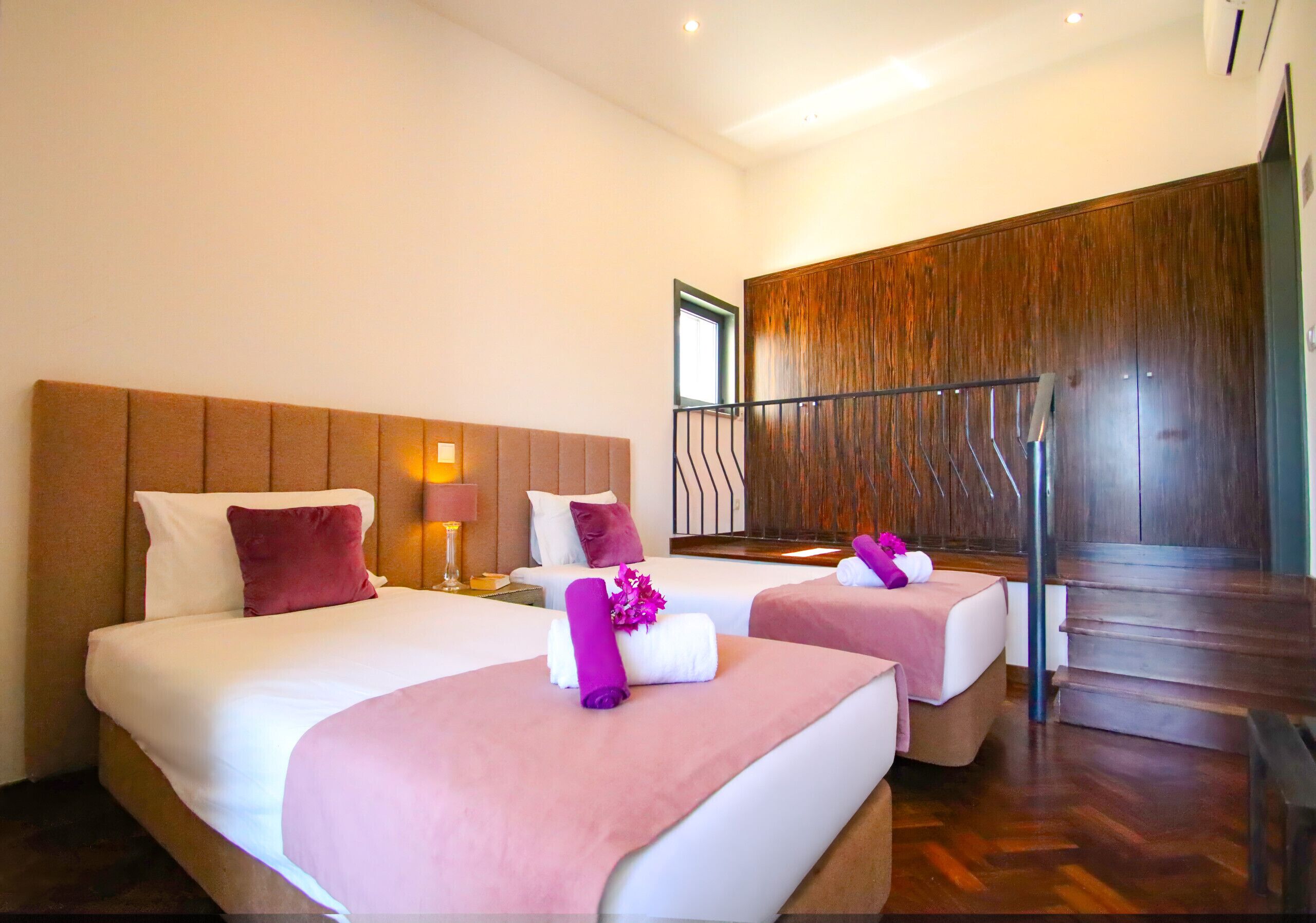 Habitación de hotel con dos camas, cabecero de madera, una escalera y una ventana.