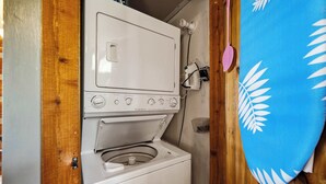 Un lavadero pequeño con lavadora y secadora, paredes de madera y una toalla azul colgada a la derecha.