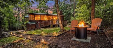 A cabin with a deck, a fire pit, and outdoor lighting.