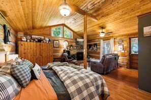 A cozy cabin interior with a bed, a fireplace, a seating area, and a wooden ceiling. - View! Hot Tub-Sauna-Fire Pit-Fireplace-Honeymoon (Sevierville)