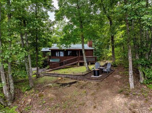 Eine Hütte, umgeben von Bäumen, mit einer Terrasse und Sitzgelegenheit im Freien.