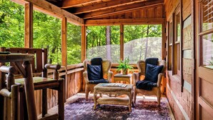 Una cabaña de madera con muebles de mimbre, ventanas amplias y vistas a un bosque.