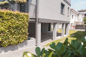 Un bâtiment moderne doté d’un balcon, d’un espace de stationnement couvert et d’une haie bien entretenue.