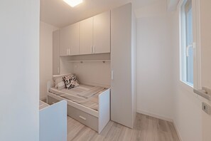 A compact bedroom with a bed, a wardrobe, and a window. - New & Modern | 200m from the beach | Balcony | Air conditioning | Sundown Living Ap 6 (Lignano Sabbiadoro)