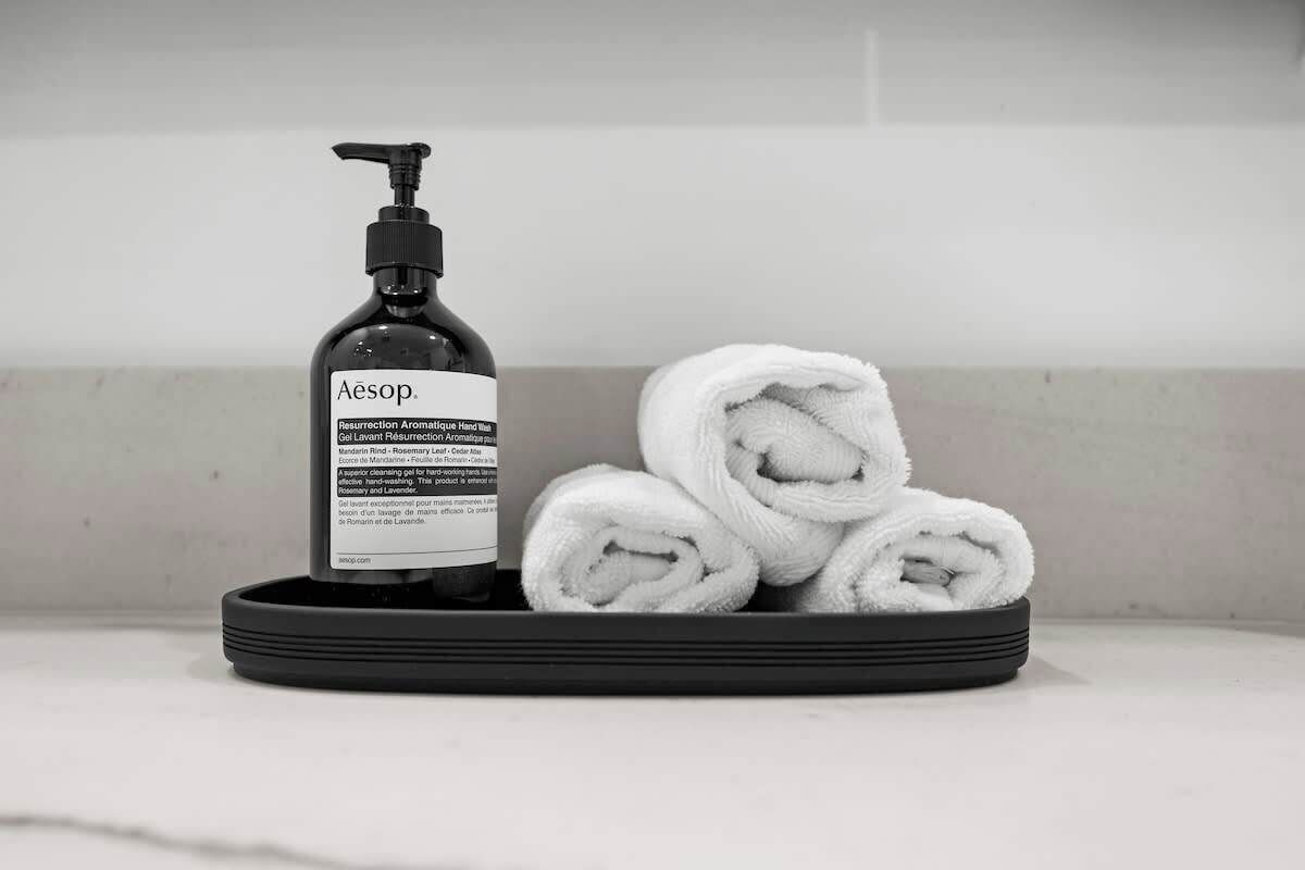 A black bottle labeled 'Aesop' and a stack of white towels on a black tray.