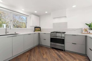 Une cuisine moderne avec des meubles blancs, une cuisinière en acier inoxydable et une fenêtre qui laisse entrer la lumière naturelle.