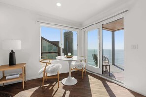 Ein Zimmer mit einem runden Tisch, Stühlen, einer Lampe und großen Fenstern mit Blick auf das Meer.