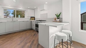 A modern kitchen with white cabinetry, a central island, and bar stools. - Oceanfront, AC, Fully Remodeled Unit (Solana Beach)