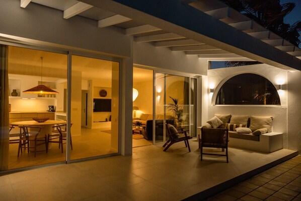 Ein moderner Außenbereich mit Essbereich, Sitzgelegenheiten und einem großen Fenster mit Blick ins Innere.