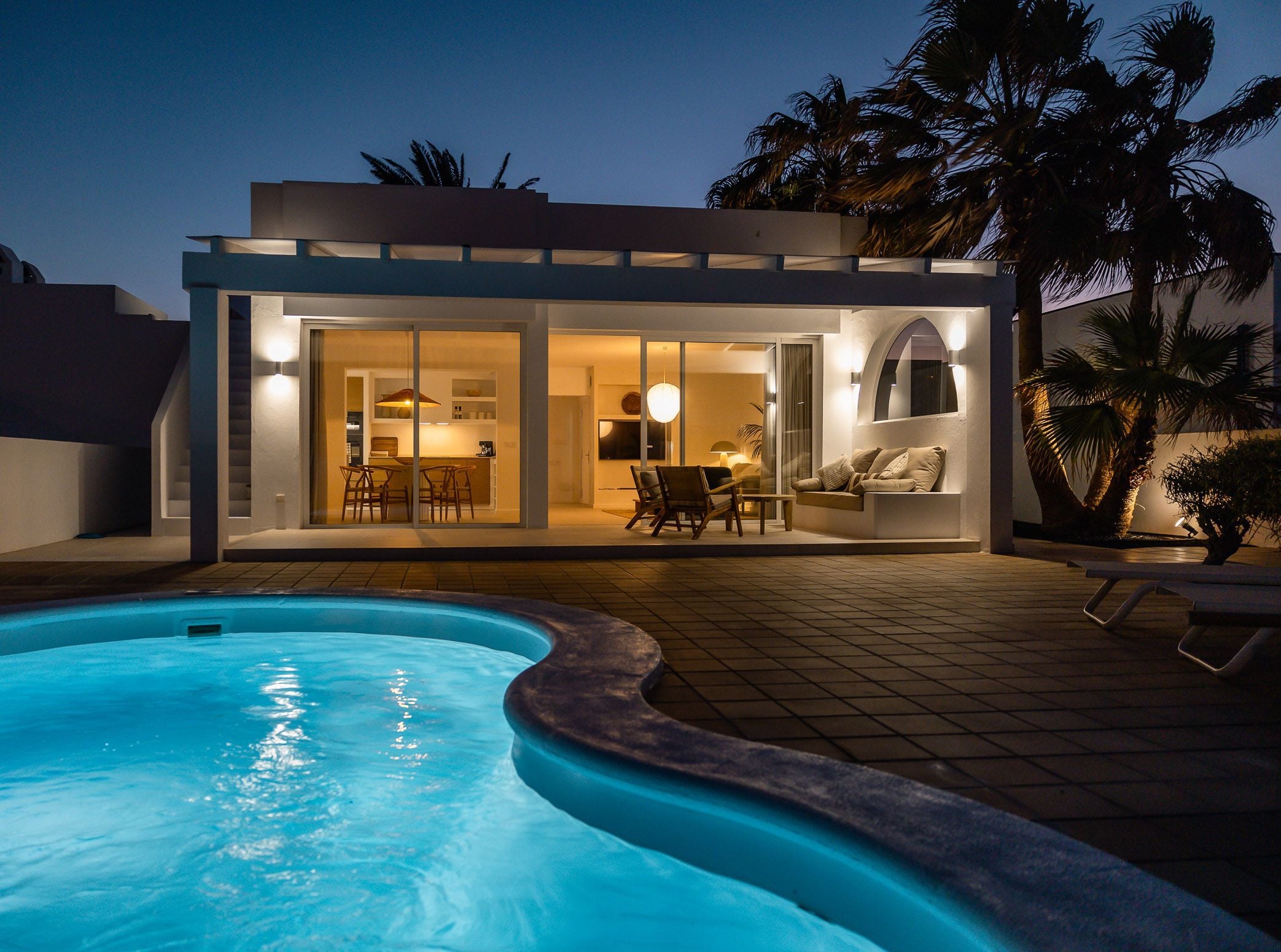 A modern house with a swimming pool, a patio with outdoor furniture, and a glass door leading to an interior space.