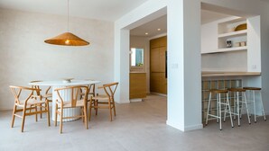 A modern kitchen with white cabinetry, a round dining table with wooden chairs, and a hanging light fixture. - Villa Playa Vista Lobos (Corralejo)