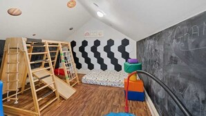 A room with a wooden play structure, a hexagonal wall pattern, and a chalkboard with writing.
