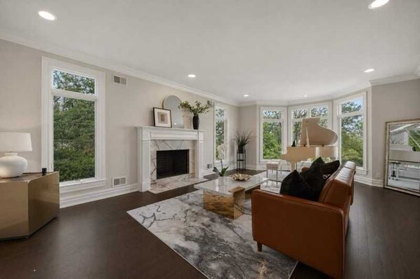 A spacious living room with a fireplace, a piano, and large windows.