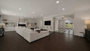 A spacious living room with a large white sectional sofa, a kitchen area with white cabinetry, and a staircase leading to another level. - Elevated Luxury Living with Sweeping NYC Skyline Views 6-bed house in Montclair (Montclair)