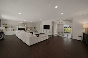 A spacious living room with a large white sectional sofa, a kitchen area with white cabinetry, and a staircase leading to another level. - Elevated Luxury Living with Sweeping NYC Skyline Views 6-bed house in Montclair (Montclair)