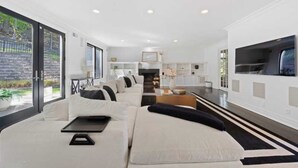 A modern living room with a sectional sofa, a flat-screen TV, and a kitchen area in the background. - Elevated Luxury Living with Sweeping NYC Skyline Views 6-bed house in Montclair (Montclair)