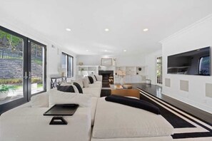 A modern living room with a sectional sofa, a flat-screen TV, and a kitchen area in the background. - Elevated Luxury Living with Sweeping NYC Skyline Views 6-bed house in Montclair (Montclair)