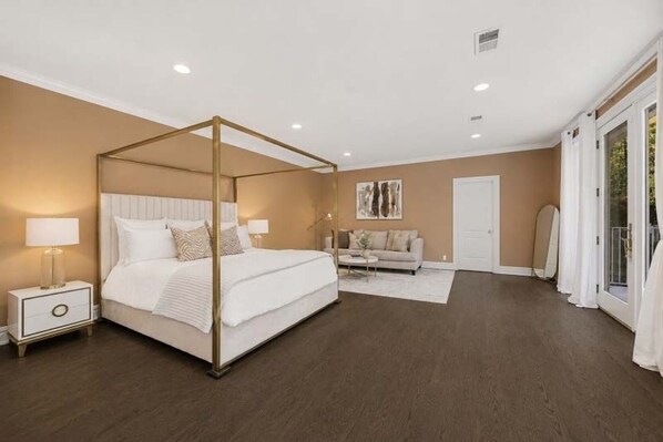 Un dormitorio con cama con dosel, una mesita de noche, un sofá y una puerta que da a un balcón.