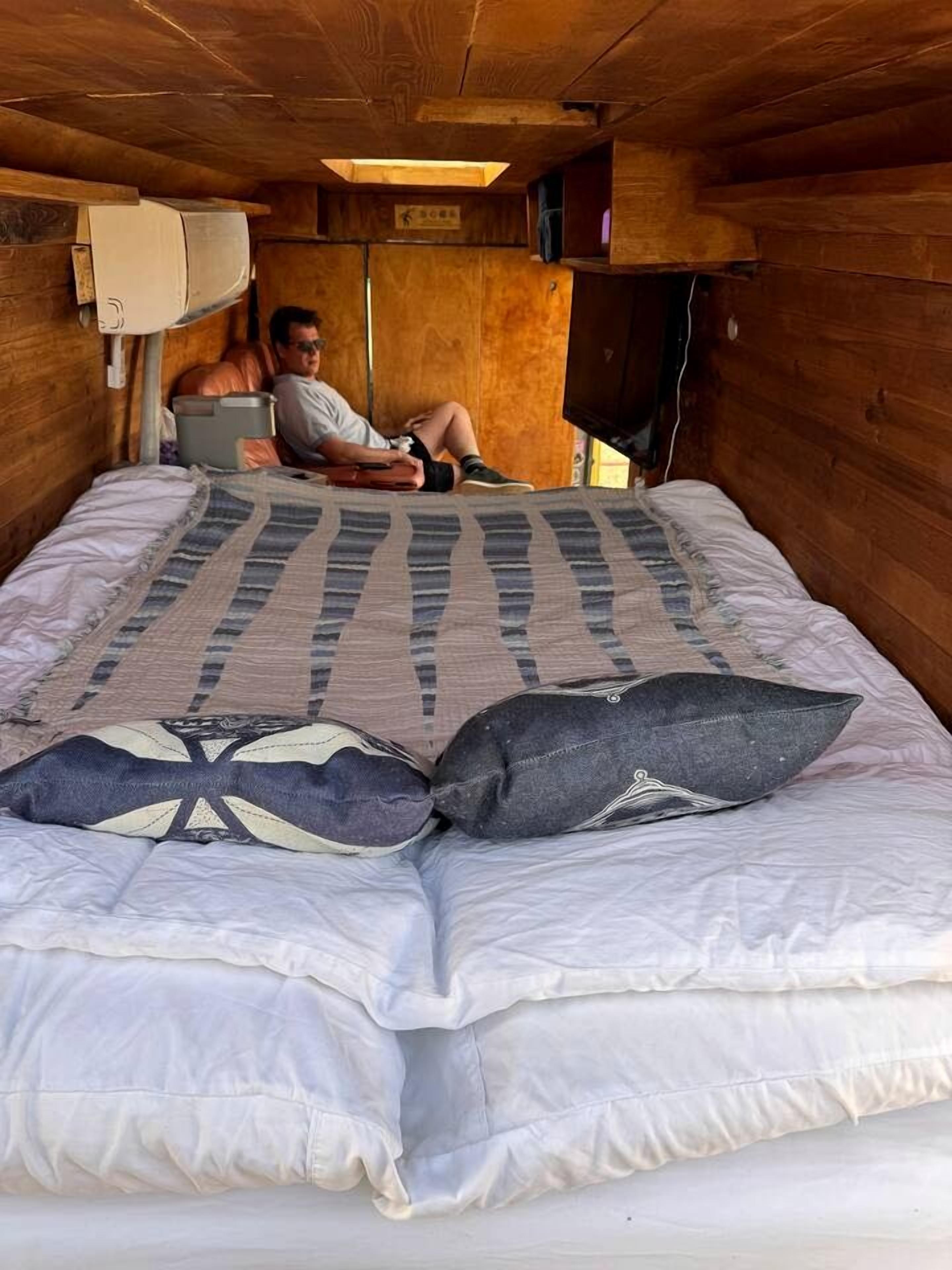 A single bed with a patterned blanket and pillows, a wooden ceiling, and a television mounted on the wall.