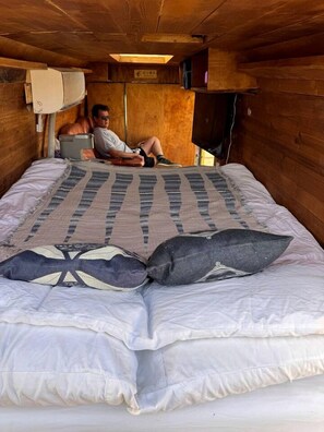 Un lit simple avec une couverture à motifs et des oreillers, un plafond en bois et un téléviseur fixé au mur.