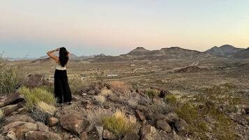 A person standing on rocky terrain with a view of a desert landscape and distant mountains.