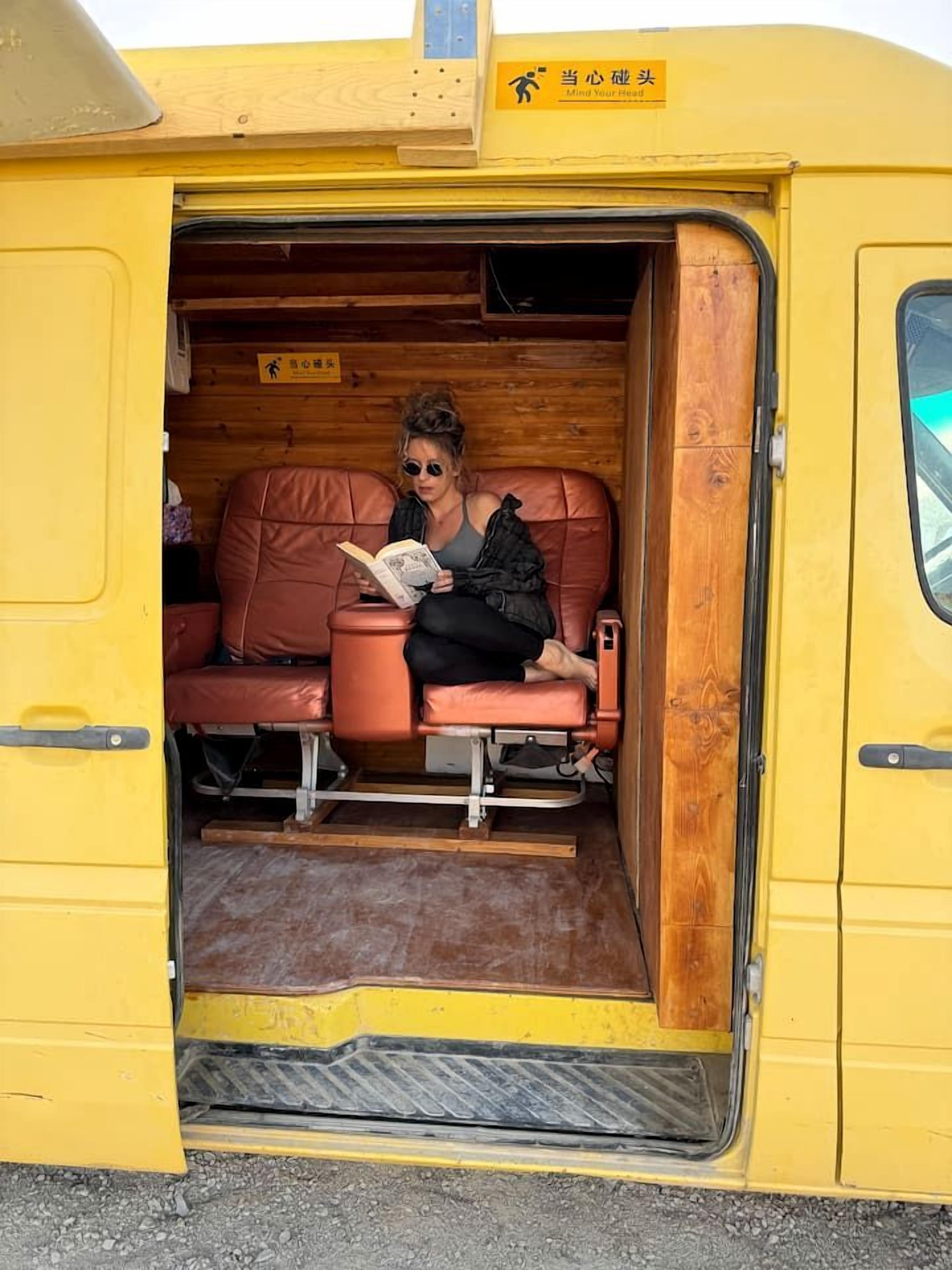 A yellow vehicle with a person seated inside, reading a book.