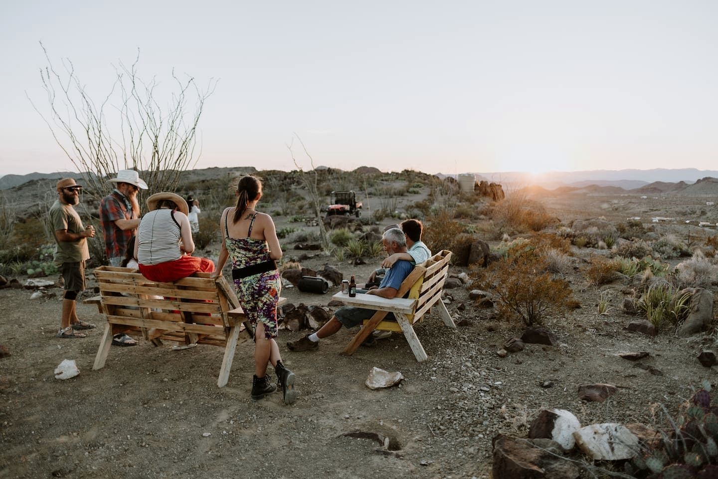 A group of people sitting on wooden benches outdoors with a desert landscape in the background.