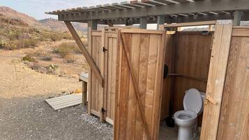 A wooden portable toilet with a closed door, set against a desert landscape.