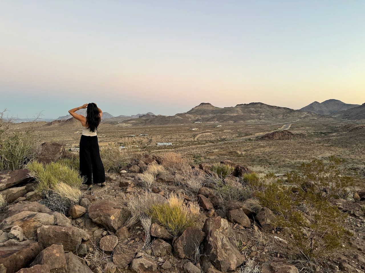 Eine Person steht auf felsigem Gelände mit Blick auf eine Wüstenlandschaft und ferne Berge.