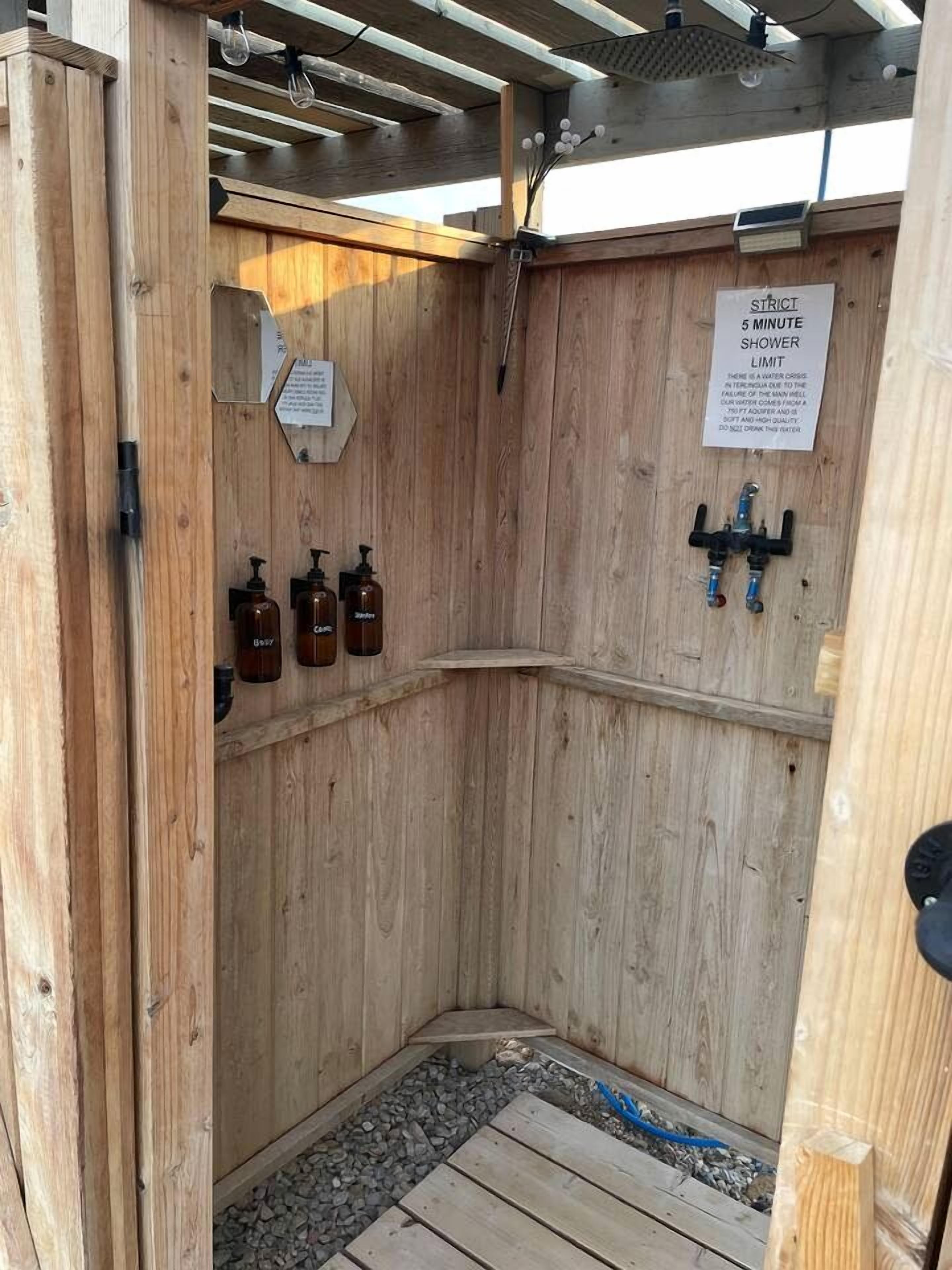 A wooden shower stall with a sign indicating a 5-minute shower limit.