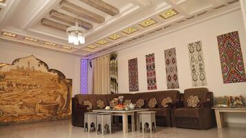 A room with a sofa set, a table with a vase, and a wall with patterned artwork.