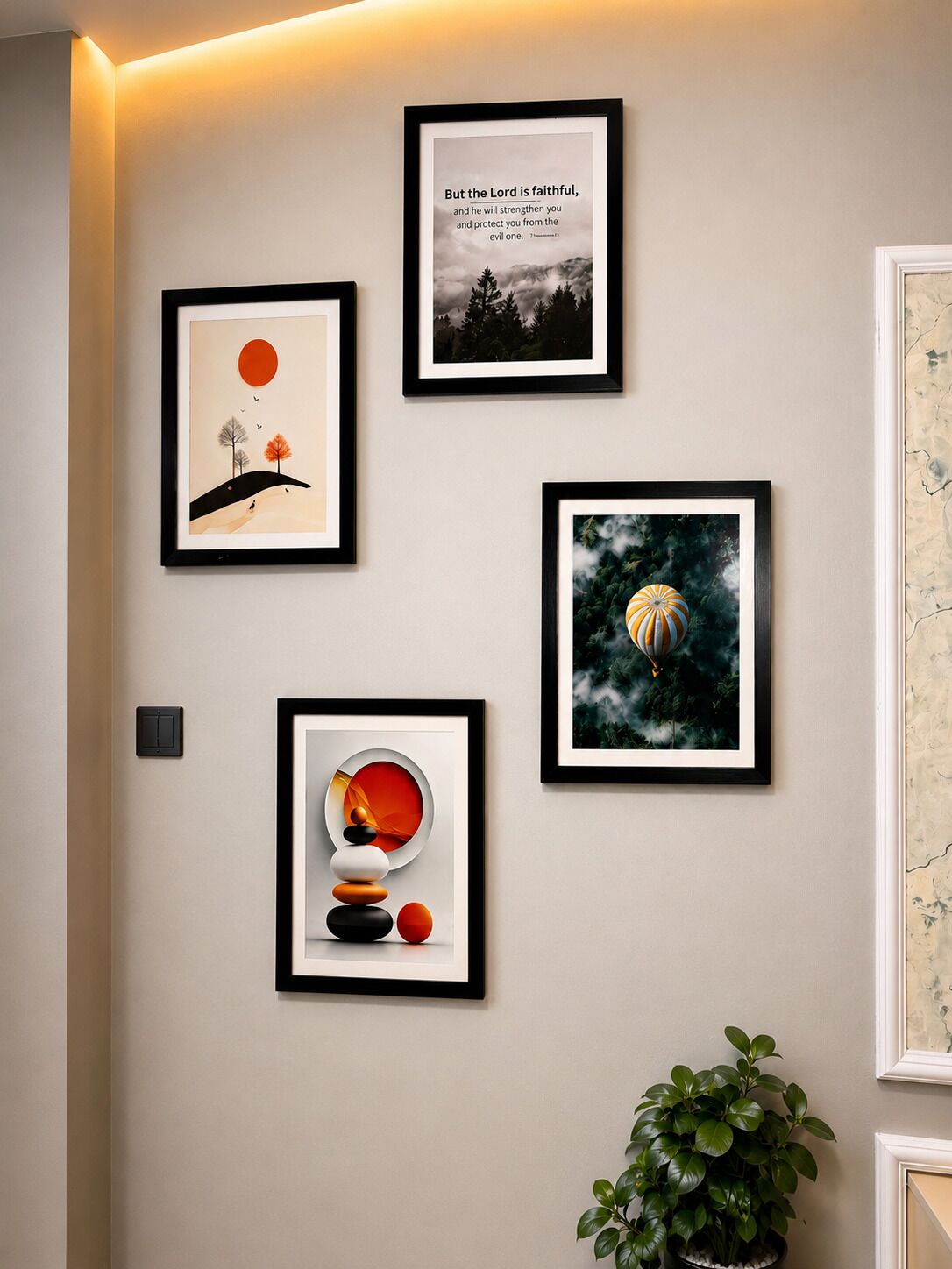 Un mur orné de quatre œuvres d’art encadrées, un interrupteur et un pot de fleurs.
