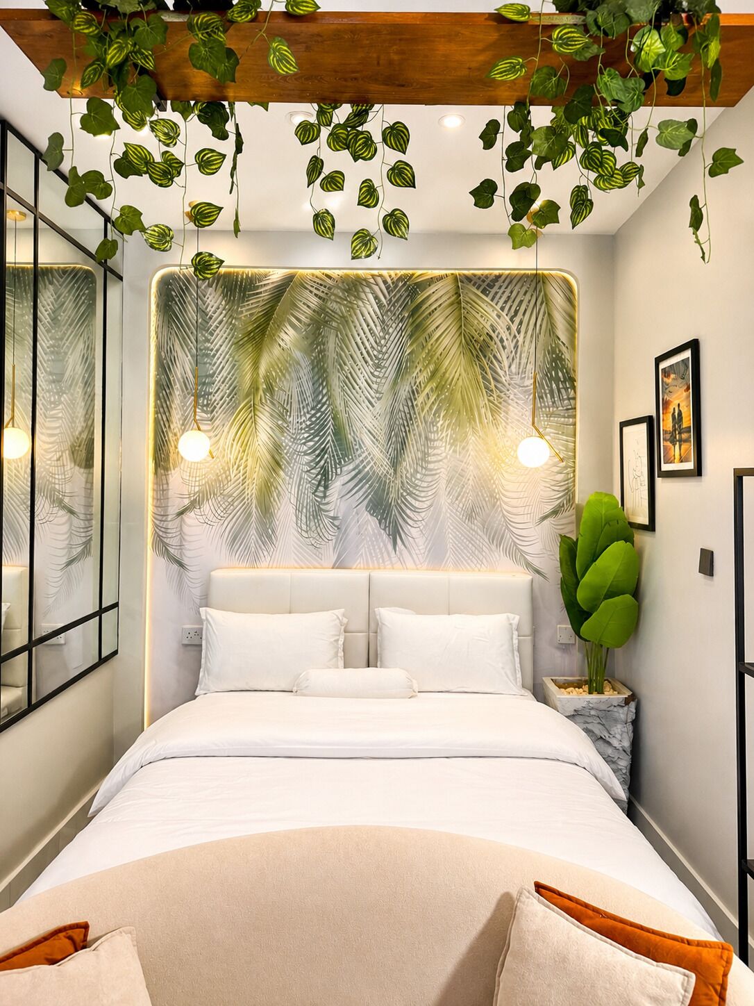 Une chambre à coucher avec un lit, du linge de lit blanc, une grande plante et un mur orné d’un motif de feuilles.