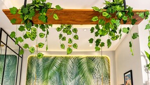 Quarto com cama, roupa de cama branca, cabeceira com padrão de folha, plantas penduradas e luminárias fixadas na parede.