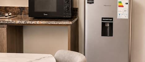 A modern kitchen with a microwave, a stainless steel refrigerator, and a marble countertop.