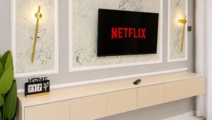 Uma sala de estar moderna com uma grande televisão de tela plana fixada em uma parede de mármore, um console minimalista abaixo e um vaso de planta à esquerda.