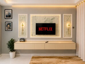 Una sala de estar moderna con un televisor montado que muestra 'NETFLIX', un mueble de pared con un reloj y obras de arte enmarcadas.