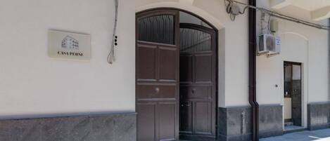 A building entrance with a large wooden door, a sign reading 'CASA PERNI,' and an air conditioning unit on the wall.