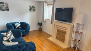 Een woonkamer met een blauwe bank, een televisie, een open haard en een plant.