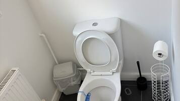A white toilet with a closed lid, a white radiator, a black floor, and a white trash bin.