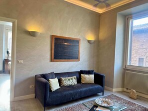 A living room with a dark blue sofa, patterned cushions, a framed artwork, and two wall-mounted lights. - Chic Rome Apartment, Master + Bonus Study/Bedroom (Roma)