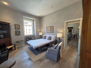 A bedroom with a bed, bedside lamps, a chair, a small table, and a window. - Chic Rome Apartment, Master + Bonus Study/Bedroom (Roma)