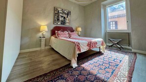 A bedroom with a bed, two bedside lamps, a chandelier, a large window, and a patterned rug. - Chic Rome Apartment, Master + Bonus Study/Bedroom (Roma)