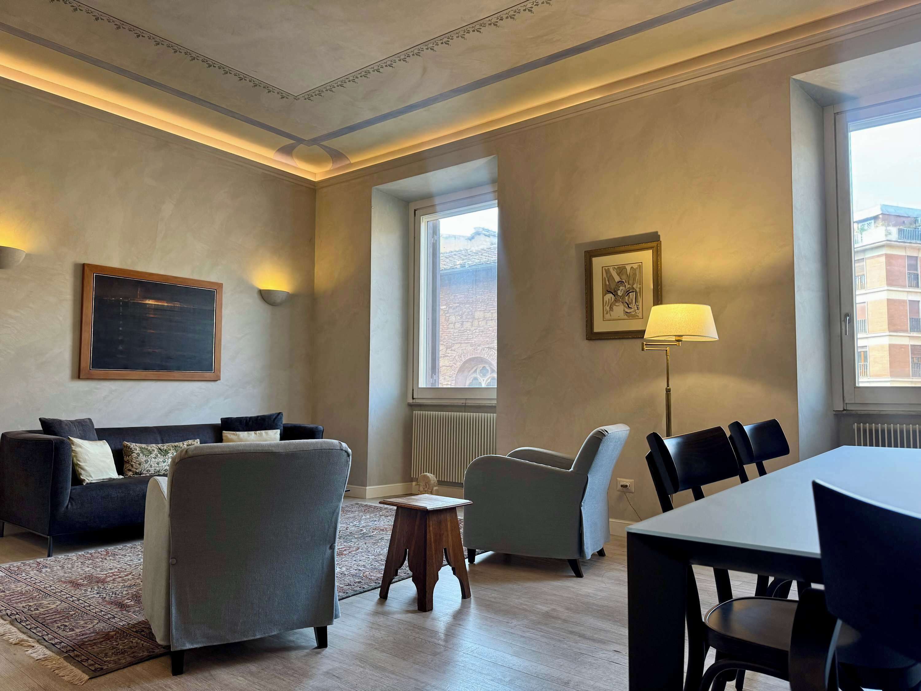Habitación de hotel con sofá, sillones, mesa de comedor y vistas a la ciudad desde la ventana.