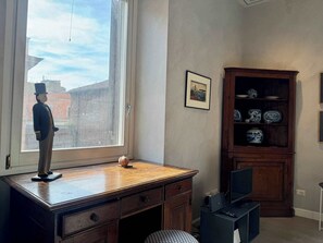 A room with a desk, a cabinet with decorative items, a window with a view of buildings, and a framed picture on the wall. - Chic Rome Apartment, Master + Bonus Study/Bedroom (Roma)